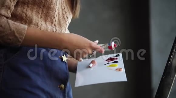 近距离拍摄一个女人的手谁挤压油漆在白色调色板视频的预览图