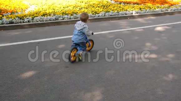 慢动作4k一个孩子在公园里骑跑步自行车一个小男孩在城市公共公园里骑平衡自行车视频的预览图