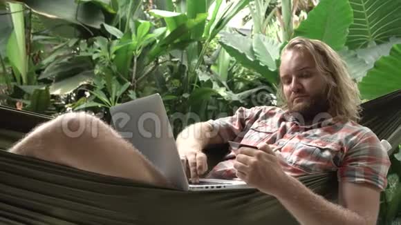 坐在吊床上用手提电脑在线银行视频的预览图