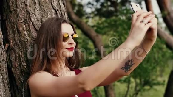 美丽的年轻女人留着长长的黑发戴着太阳镜自拍日落时在公园里慢节奏视频的预览图
