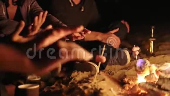 年轻人在海边坐在篝火旁野餐晚上热身特写视图视频的预览图