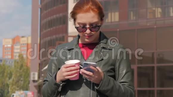 年轻的女人在街上喝咖啡打字发手机短信在城市里散步视频的预览图