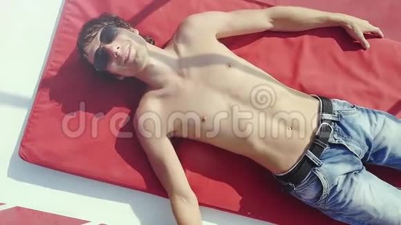 戴着太阳镜的性感年轻人在暑假里可以放松下来躺在游轮上晒成棕褐色视频的预览图