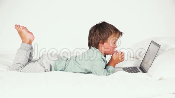 4岁男孩躺在床上玩笔记本视频的预览图