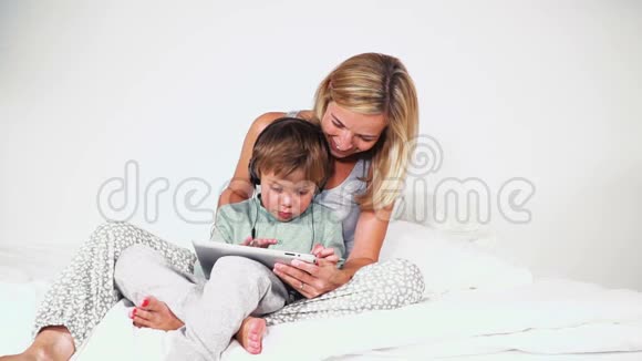 4岁的男孩和妈妈躺在床上玩平板电脑视频的预览图