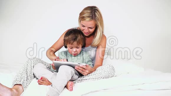 4岁的男孩和妈妈躺在床上玩平板电脑视频的预览图