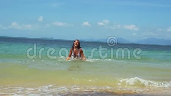 阳光明媚的夏日穿着比基尼的年轻女子沿着异国情调的海滩奔跑在海里游泳慢动作视频的预览图
