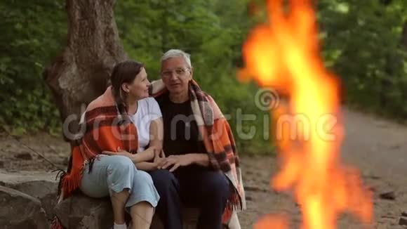 一对老夫妇坐在树林里的篝火旁视频的预览图
