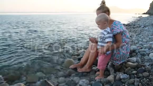 日落时分母亲和儿子坐在海滩上视频的预览图