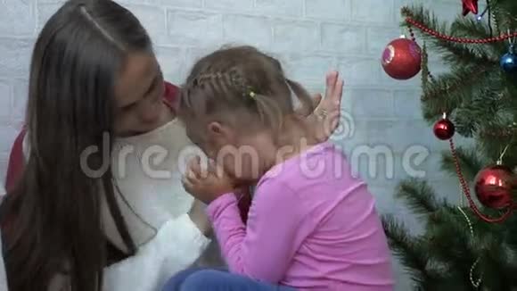 年轻的母亲抱着她哭泣的小女儿在圣诞树旁视频的预览图