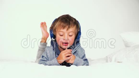 4岁男孩躺在床上带着耳机玩平板电脑视频的预览图