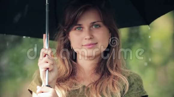美丽的女人站在雨中的伞下真诚地笑着享受大自然视频的预览图