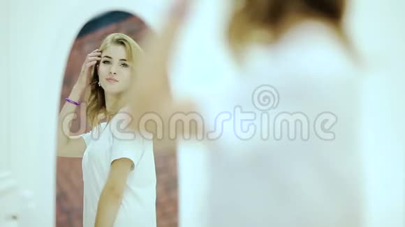 美丽的年轻女子穿着白色衬衫看着镜子里的倒影视频的预览图