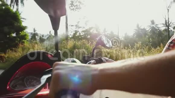 在热带阳光明媚的道路上驾驶摩托车的摩托车旅行者的轮子上的人的手的特写镜头视频的预览图