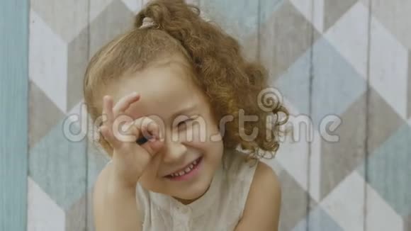 一个长着红色卷发的漂亮小可爱的小女孩展示了一个望远镜展示了一个问候的标志在一个视频的预览图