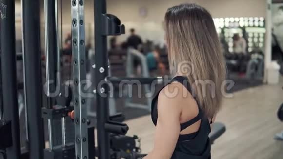 一个年轻的健身女子在健身房用训练机做二头肌运动视频的预览图
