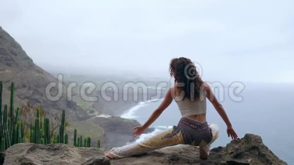 一个女人坐在悬崖边上摆出一副俯瞰大海的姿势举起双手吸气视频的预览图