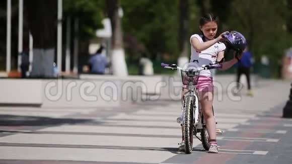 可爱的女孩戴着头盔然后在阳光明媚的日子骑自行车在公园里视频的预览图