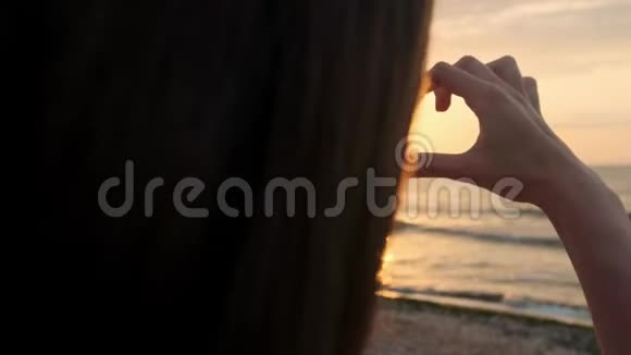下面的动作结束无法辨认的女人用她心形的手指捕捉夕阳年轻的女孩视频的预览图