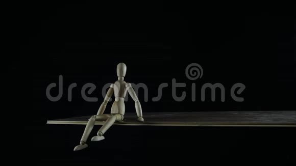 停止动作的木人形假人在黑背景的工作室里拖拖拉拉地坐着挥舞着双腿拿头衔视频的预览图