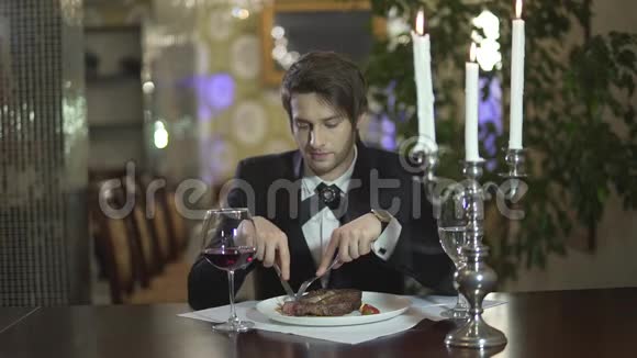 年轻英俊的黑发胡须蓝眼睛男人穿着经典的燕尾服切肉牛排在餐馆吃晚餐视频的预览图