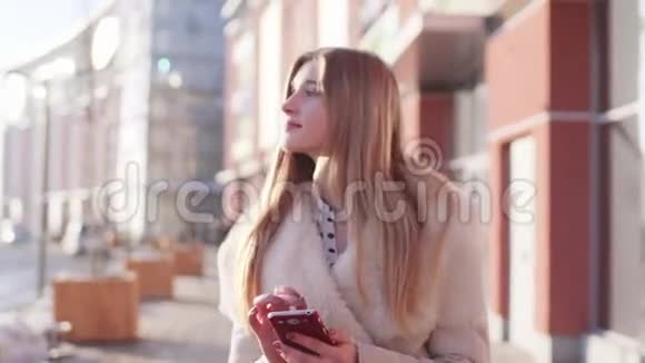 年轻漂亮的金发女孩走在繁忙的街道上一边在手机上看书屏幕上打信息视频的预览图