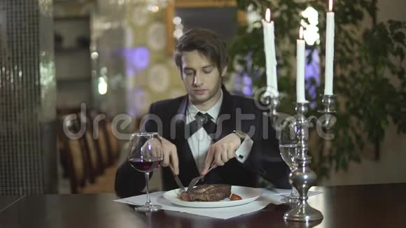 年轻男子穿着经典的燕尾服切肉牛排在餐厅享用晚餐视频的预览图