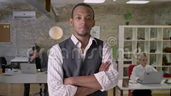 年轻的非洲商人站在办公室里双臂交叉看着镜头同事们正在与他合作视频的预览图