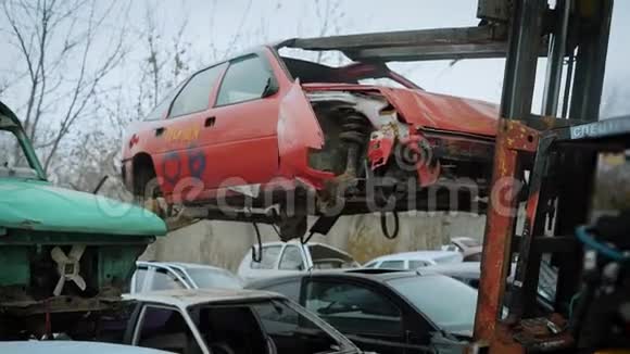 在阴天的秋天里装卸机正在上升把一辆破旧的红色汽车卸在垃圾场里视频的预览图