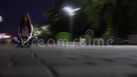 一个穿着衬衫和牛仔裤的迷路女孩坐在广场的晚上在散步的人中间用模糊的时间拍摄视频的预览图