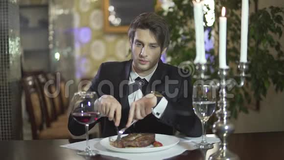 穿着经典的燕尾服切肉牛排在餐厅享用晚餐的英俊年轻的黑发胡须蓝眼睛男人视频的预览图