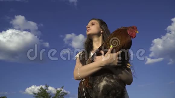布鲁内特手里拿着公鸡背景是云彩乡村生活视频的预览图