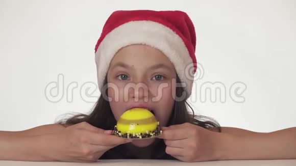 戴着圣诞老人帽子的漂亮女孩有胃口很高兴在白色背景股票上吃生日蛋糕视频的预览图