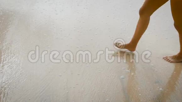 穿着黑色泳衣的漂亮女孩在潮湿的沙滩上留下一条小径年轻女子腿苗条晒黑视频的预览图