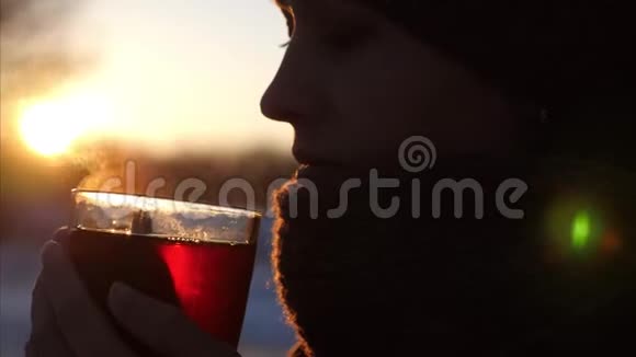 年轻美丽的女人在夕阳美丽的太阳下喝着透明玻璃的茶视频的预览图