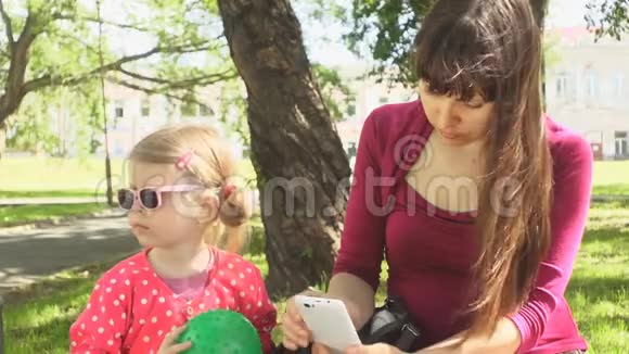 在公园里妈妈和女儿享受着电话的微笑享受着共同的时光视频的预览图