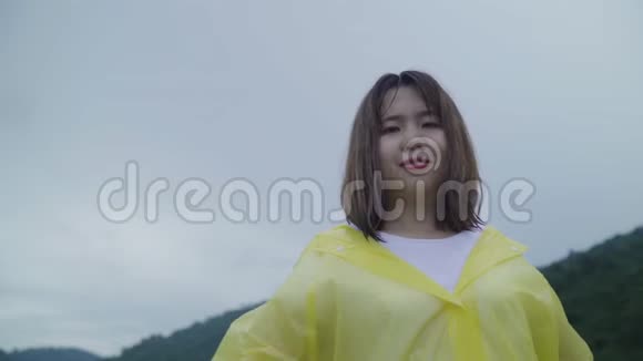 慢动作年轻的亚洲妇女感到高兴的打雨而穿着雨衣走在森林附近视频的预览图