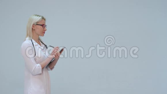 女医生在剪贴板上写字在灰色背景下微笑视频的预览图