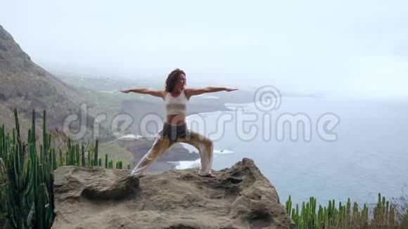 女人冥想瑜伽战士在海洋海滩和岩石山的姿势激励和鼓舞人心的健康和视频的预览图