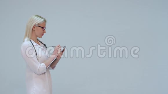 金发医生在剪贴板上写字在灰色背景下微笑视频的预览图