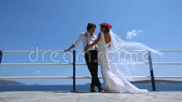 海滩上美丽的新郎新娘面纱新娘在风中翩翩起舞视频的预览图