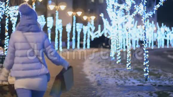 快乐的女孩带着包裹在冬天的夜灯公园散步视频的预览图