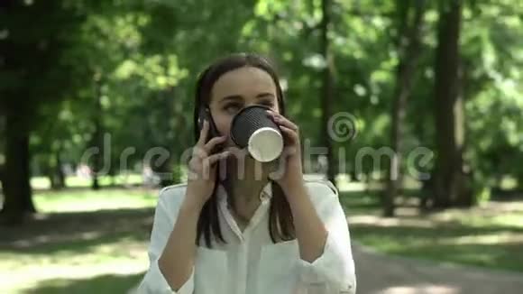 女人喝咖啡在公园里用手机说话视频的预览图