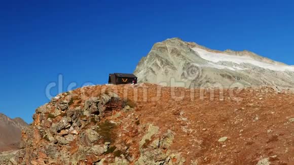 女人到达山顶上的山屋在高空岩石景观中背景是冰川和山峰历险记视频的预览图