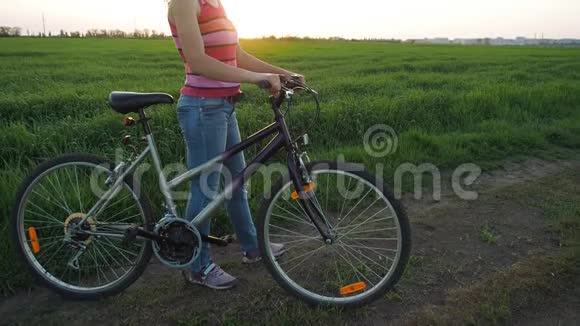 日落时骑自行车的女孩在城市背景下一个在田野里骑自行车的女人全国的体育女孩视频的预览图