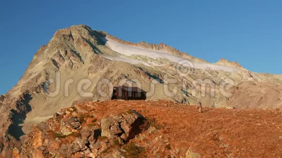 女人到达山顶上的山屋在高空岩石景观中背景是冰川和山峰历险记视频的预览图