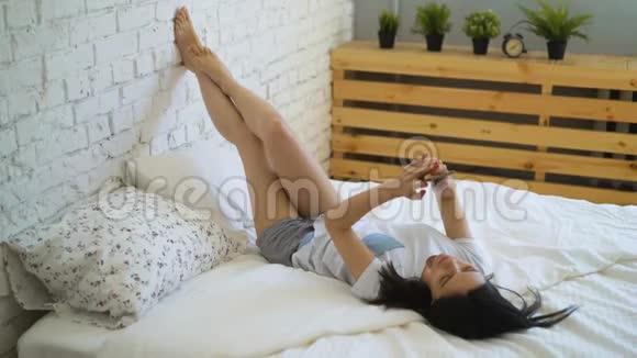 年轻女子躺在床上用智能手机视频聊天视频的预览图