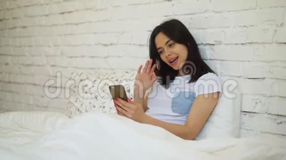 年轻女子躺在床上用智能手机视频聊天视频的预览图