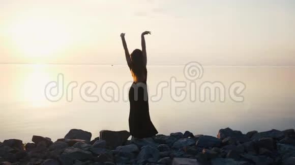 穿着黑色长裙在日落时分在沙滩上跳舞的无忧无虑的女人视频的预览图