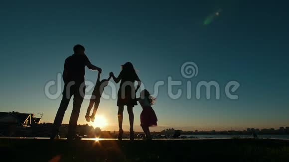 幸福的家庭父亲母亲女儿和小儿子日落时的剪影慢动作视频的预览图